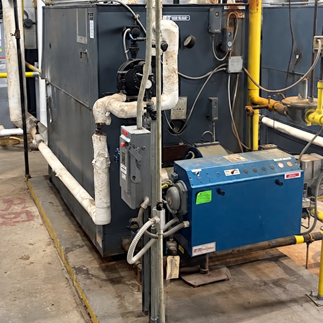 Commercial boiler with a blue burner box and insulated piping in a boiler room