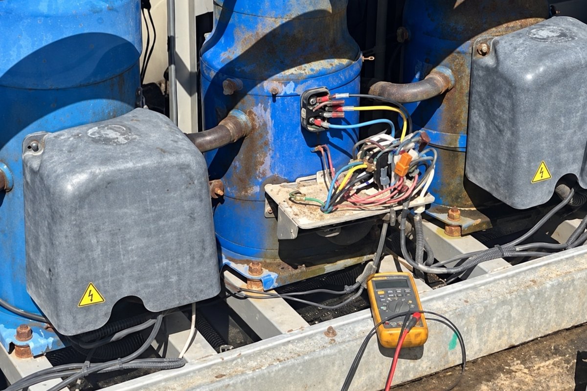Blue compressors and open wiring inside a condensing unit with a multimeter attached