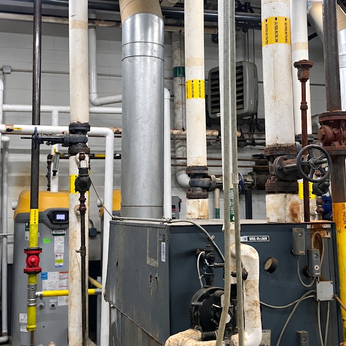 Insulated glycol pipes, flanged valves and a commercial boiler in a mechanical room