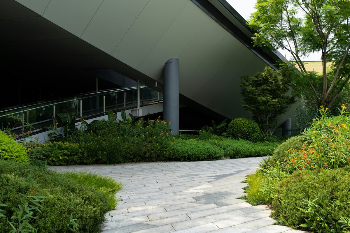 Curving stone paving walkway through lush green shrubs and orange flowers beside a modern building