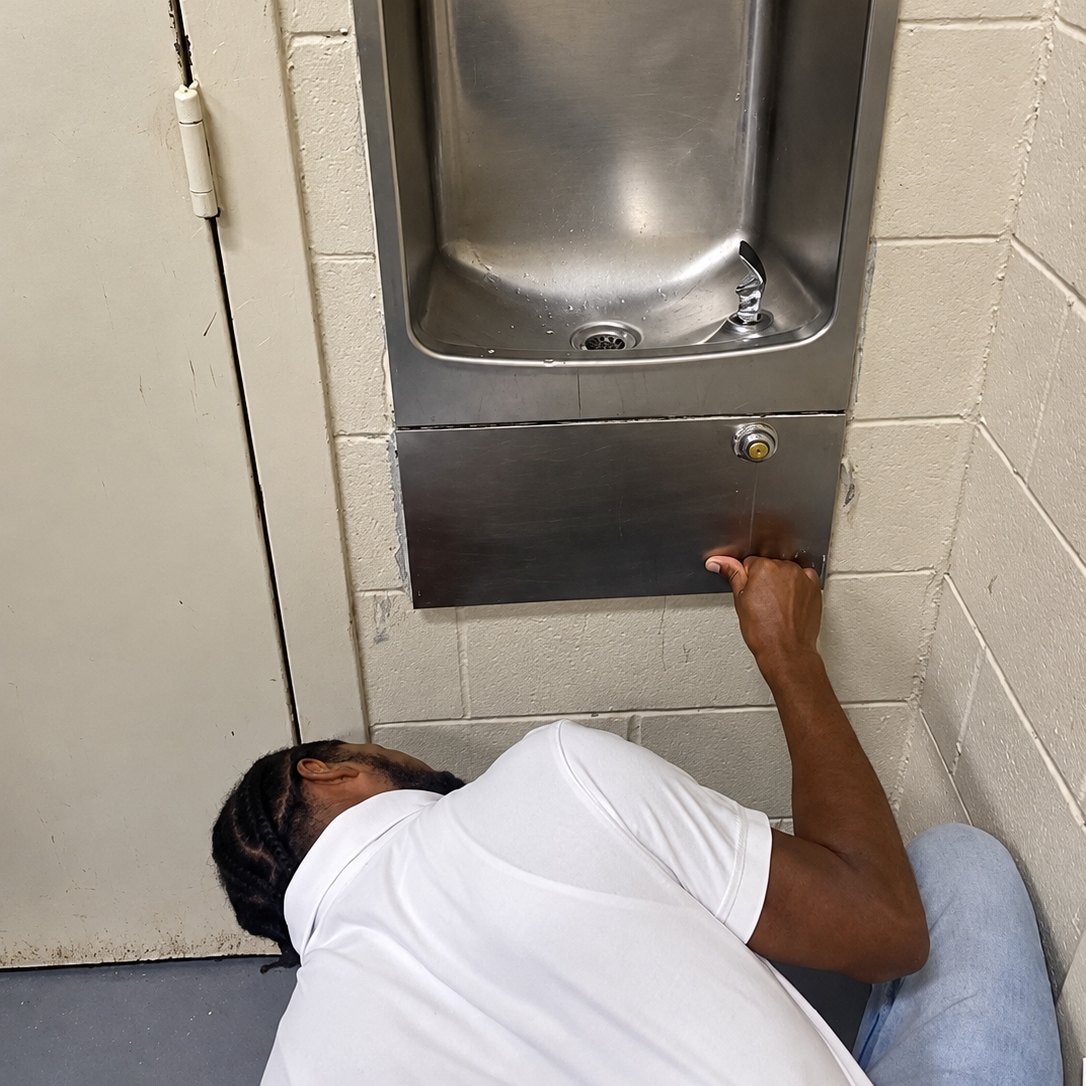 Technician reaching under a stainless wall-mounted drinking fountain