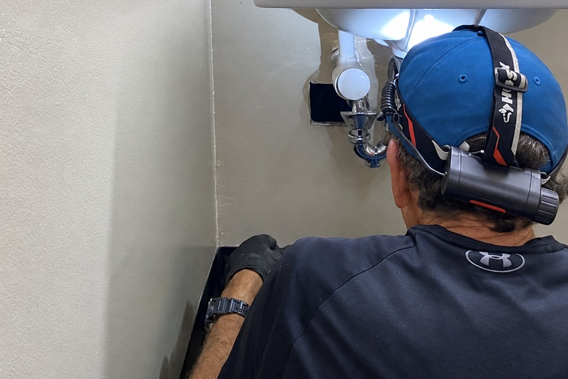 Technician with a headlamp working on the drain under a restroom sink