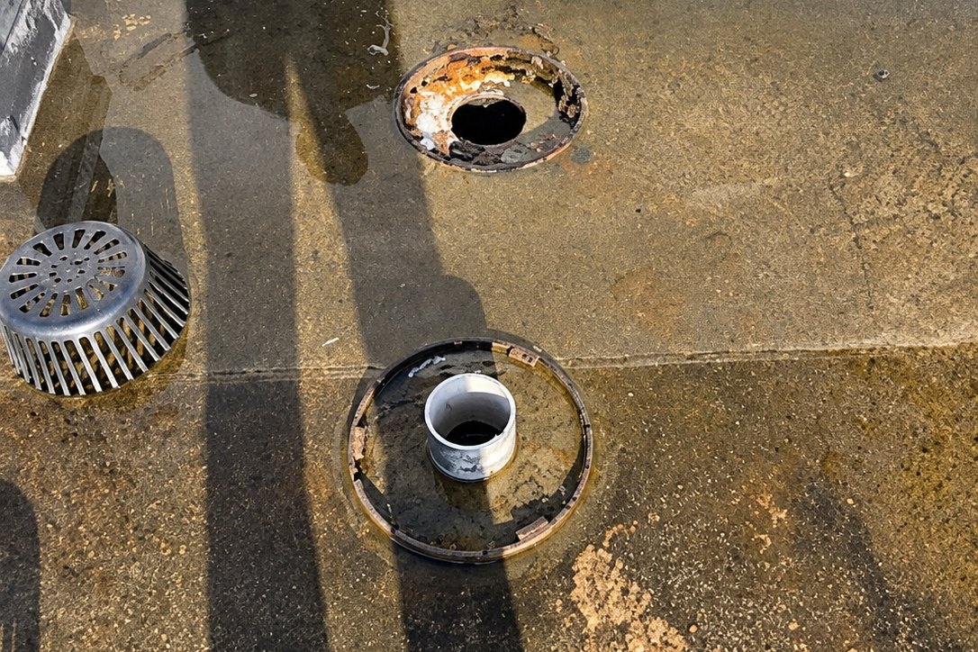 Two roof drains with strainers removed on a stained flat roof