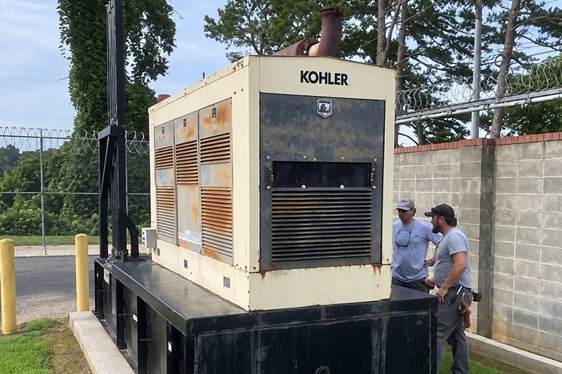 Two technicians beside a large standby generator inside a fenced gear yard