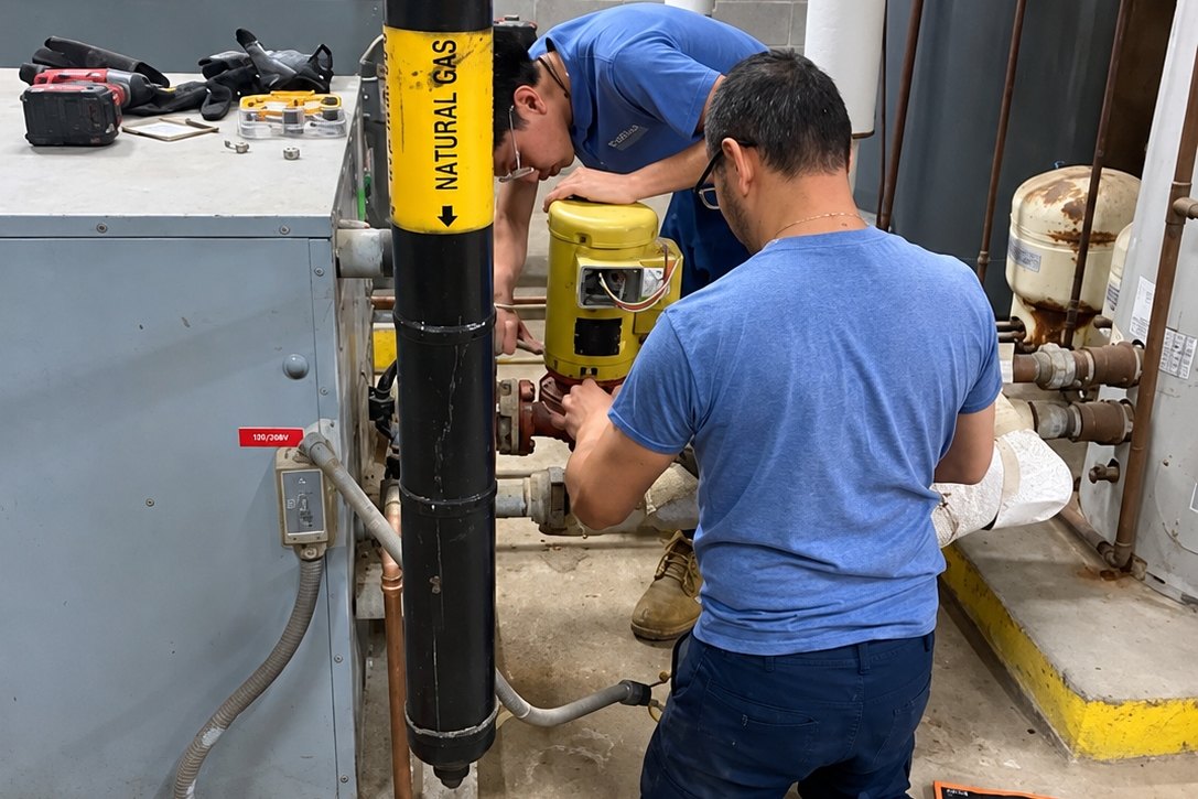 Two technicians working on a circulator pump beside a natural gas line