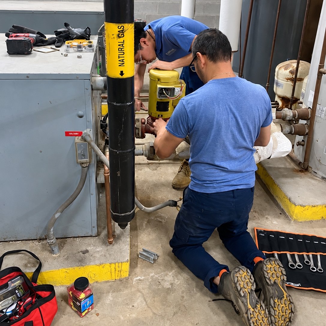 Two technicians working on a boiler room pump with hand tools laid out