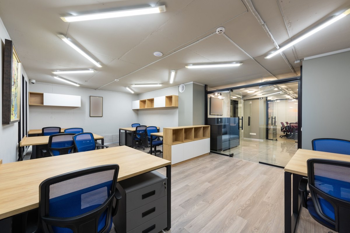 Open commercial office with desks, blue chairs, ceiling light fixtures and glass partition doors