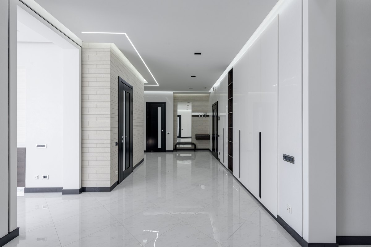 Bright commercial hallway with smooth white walls, dark doors and a glossy white tile floor