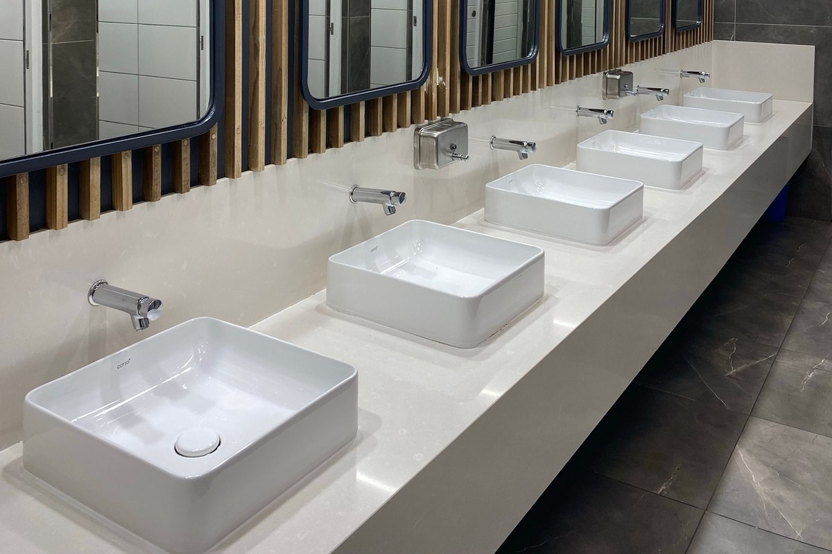 Row of white countertop sinks with wall-mounted taps and framed mirrors in a modern commercial restroom