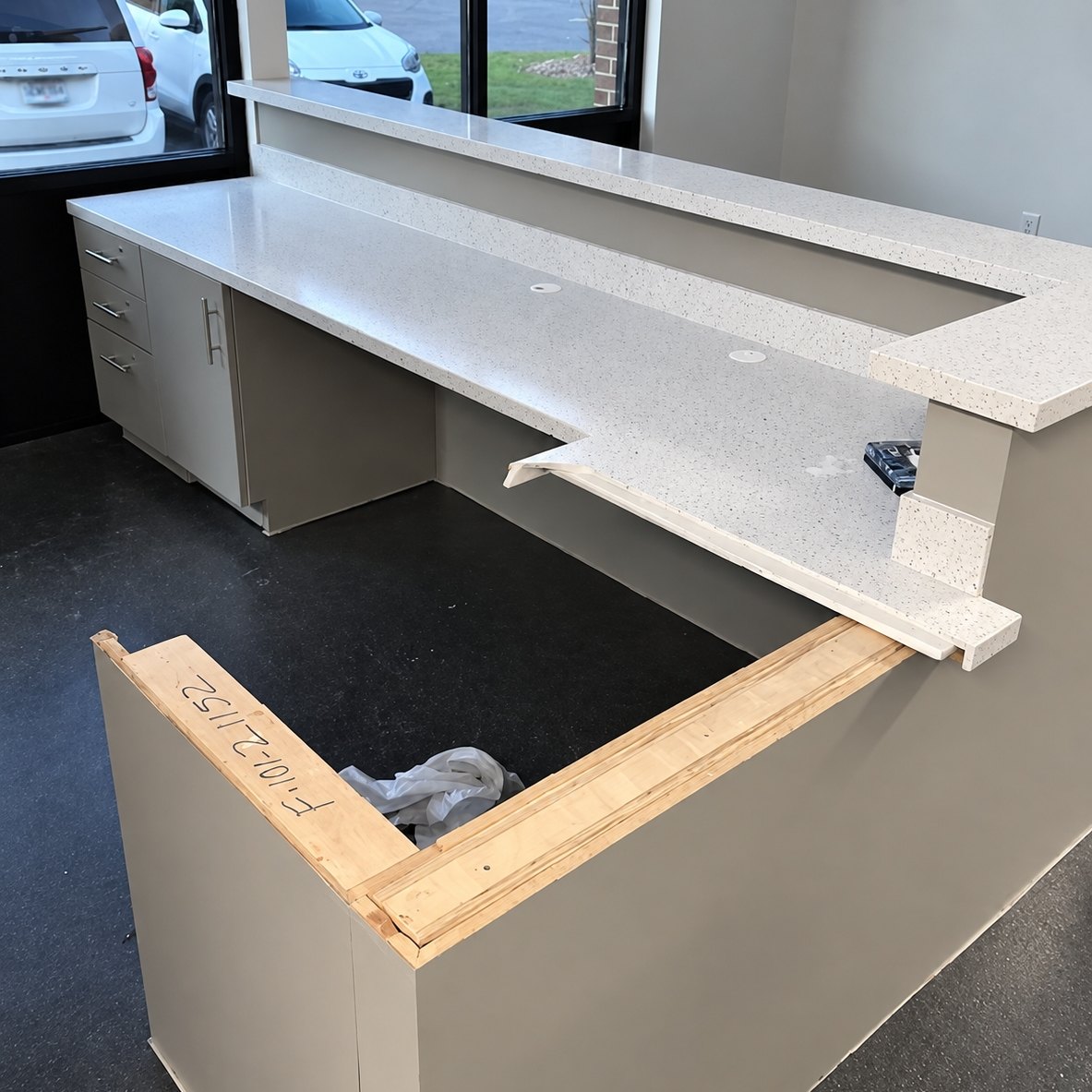Reception desk with a speckled white countertop and tan base cabinets beside a large window in a commercial building
