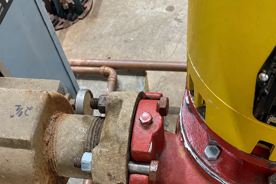 Red pump flange bolted to a corroded pipe fitting under a yellow motor