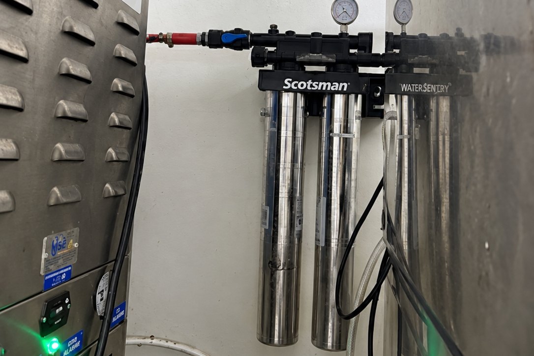 Wall-mounted water filter cartridges with pressure gauges beside a stainless gear cabinet